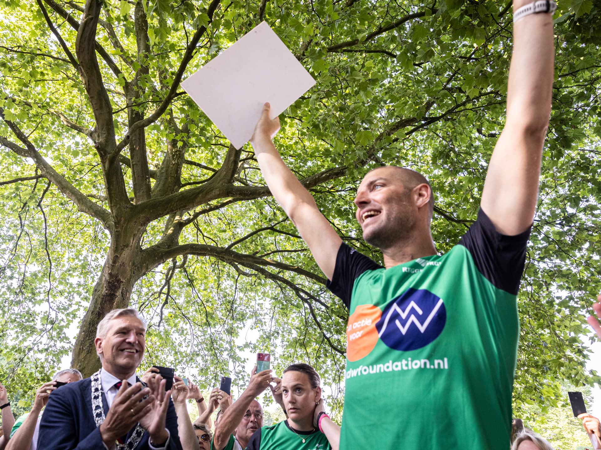 Maarten juicht met de armen omhoog tussen publiek, in een shirt van zijn foundation