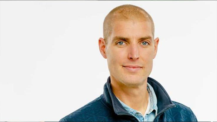 Portret van Maarten van der Weijden in een blauwe jas tegen een witte achtergrond